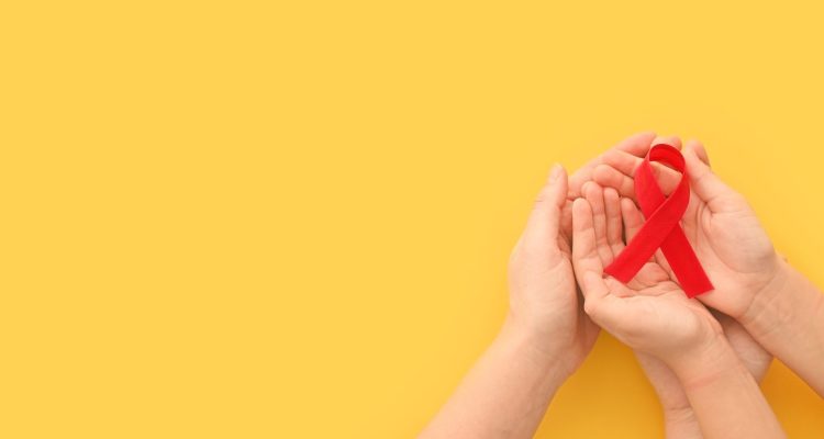 Concept World AIDS Day. Hands of woman holding red ribbon on yellow background. Blood transfusion and donation. Hemophilia day. World Health Day. Layout. Copy space. Banner. top view